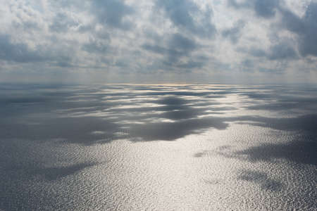 Gray beautiful clouds over the sea. Long panoramic sea autumn view. Low Cumulus clouds and bright sunlight. Shadow of clouds on the surface of the water. Gray steel natural shades of the autumn sea.の写真素材