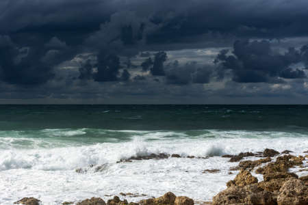 A violent storm in the sea. Beautiful blue storm clouds. A cloudy, menacing landscape. A terrible storm warning. Waves break on the rocky shore.の写真素材