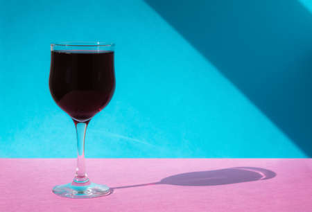 A glass of wine on a multicolored background. Bright colorful minimalism. Hard sunlight and a long...