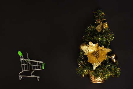 Christmas tree on a black background and the shopping cart view at the top. The concept of buying...