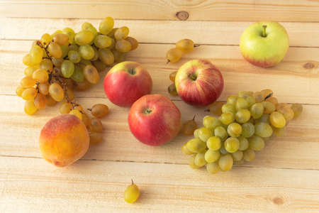 Grapes, apples and peaches on the background of natural wood. Top view of a juicy rustic fruit composition. Autumn harvest on a wooden table. Healthy diet. Vitamin complex.の写真素材