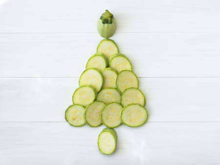 Christmas tree silhouette of zucchini on a white wooden background. Cut parts of zucchini in the form of a Christmas tree. Creative composition on the theme of diet food and Christmas. Flat lay food.の写真素材