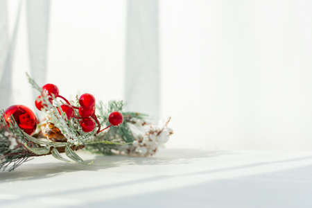 Christmas twig on a white wooden background. Christmas holiday design with a snow-covered spruce twig with red balls and red berries. Natural bright sunlight. Top view, flat layout, copy spaceの写真素材