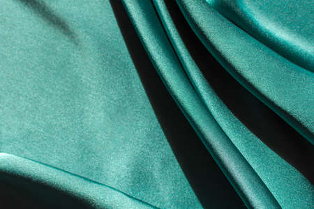 Green satin fabric pleats close-up. Abstract trend background of Tidewater Green color. Luxury elegant bright texture with hard light with copyspace. Banner design for Christmas, Valentine's dayの写真素材