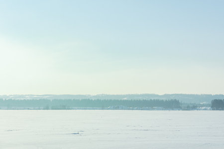 Winter landscape with field, trees and blue sky,long horizontal composition. Light fog and haze over the forest. Natural atmospheric cold background. View from the car window on the snow-covered treesの写真素材