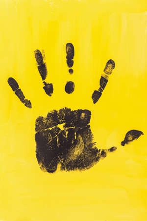 A black handprint on a yellow background. Abstract creative layout in contrasting colors with acrylic paint. The concept of freedom, creativity, inspiration. Monochrome drawing vertical composition.の写真素材