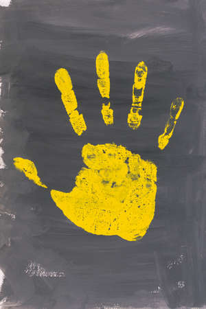 A yellow handprint on a gray background. Abstract creative layout in contrasting colors with acrylic paint. The concept of freedom, creativity, inspiration. Monochrome drawing vertical composition.の写真素材