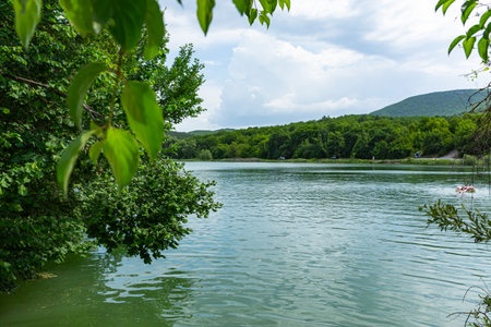 Summer lake surrounded by green trees. A place of recreation in nature. The concept of summer, vacation, happy pastime. Fresh clean air, warm water, people bathe. Life in the country, a rustic motif.の写真素材