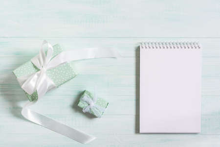 Gifts in a package with a white satin ribbon, a notebook on a wooden mint background. Top view, flat...