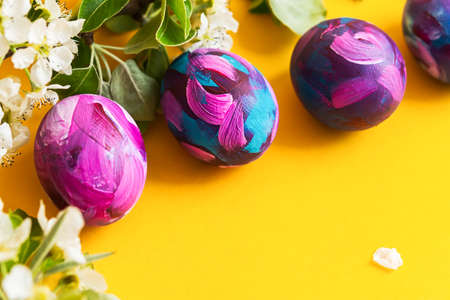 Easter eggs painted with acrylic, a sprig of a blooming pear on a yellow background. Happy Easter. Hand-painted Easter eggs close-up view from above. Flat layout, bright colorful monochrome backgroundの写真素材