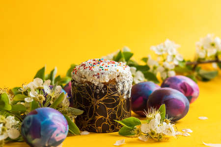 Easter cake, painted eggs and a sprig of a blooming pear on a yellow monochrome background. Happy...