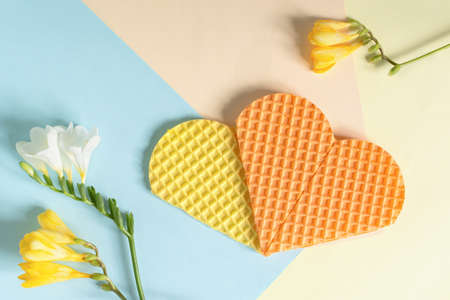 Mother's Day. Greeting card with yellow and white flowers. Flat layout with two waffle hearts. Delicate pastel pink, beige and blue background. Beautiful spring design, creative compositionの写真素材