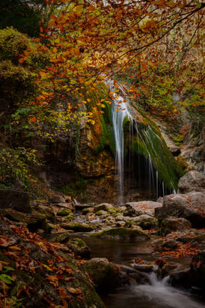 Autumn Jur Jur waterfall in the Crimea. Beautiful atmospheric sunny landscape. A small waterfall falls from the mountain on a stone in green moss. Golden leaves on the trees, a fabulous place. Travelの写真素材