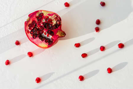 Pomegranate fruit with scattered grains on a white background top view. An authentic composition in sunlight and shadows. Water droplets on the seeds. Dietary product, proper nutrition. Copy spaceの写真素材