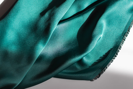 Blue-green satin fabric. Smooth silk fabric cut off on the table. Shiny soft folds in selective focus. Dark turquoise color of the sea wave. Deep rich design for covers, websites, sewing workshops.の写真素材