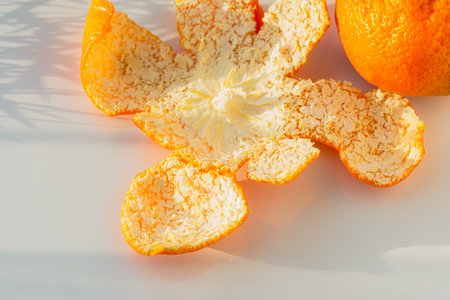 Tangerines peeled peel on a white table close-up. Juicy sweet tropical fruits for the New Year holidays. The concept of Christmas, winter mood. Mandarins in soft focus, sunlight and natural shadowsの写真素材