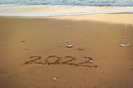2022 Happy New Year inscription sand beach. The written text is written on yellow sand and is washed...