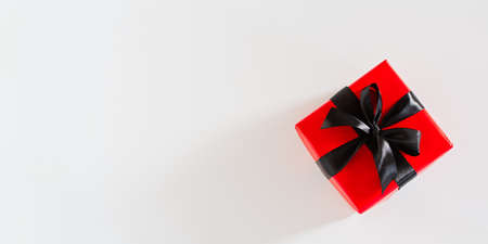Gift black and red packaging. Top view of a bright gift with a black satin ribbon on a white background. Conceptual minimalistic banner design for Birthday, Christmas, Valentine's Day. Copy spaceの写真素材