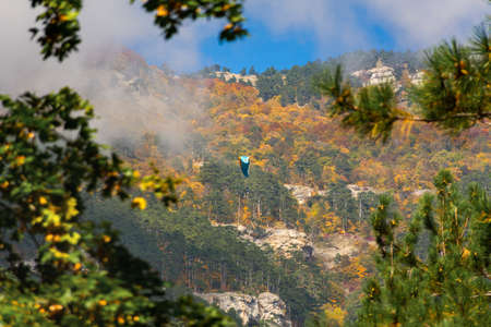 Paraglider autumn mountains. Autumn adventures in the mountains, the concept of an active lifestyle, freedom. Flying on a blue parachute alone. Extreme sport, recreation. Unrecognizable personの写真素材