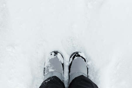 Feet snow top view. Winter gray boots stand on white snow. Textured background. Women's suit black pants and boots for walking, hiking, trekking. The concept of winter holidays, weekends, snowfall.の写真素材
