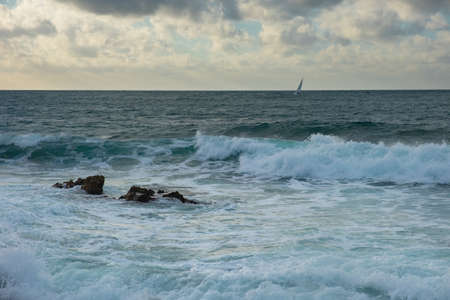 Turquoise sea stone beach, breaking waves on a cloudy spring day. Beautiful sea background. The...