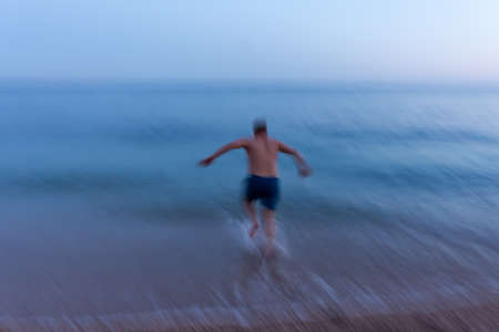 Blurred movement of the man of the sea. Abstract background of a man jumping into the water. Blue seawater on long exposure. Conceptual summer minimalism. Funny movement. Summer holidays, vacationsの写真素材