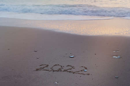2022 Happy New Year inscription sand beach. The written text is written on yellow sand and is washed...