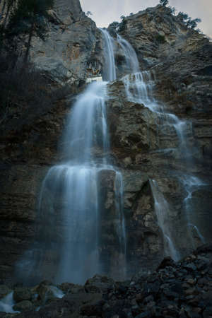 Uchan-su waterfall in the Crimea in winter. Uchan-su waterfall on Ai-Petri Yalta mountain. blurred movement of water. A majestic high sheer cliff with falling water. Waterfall texture. rapid flowの写真素材