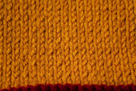 Knitted texture background. Hand-knitted wool. Macrophotography of a thread drawing. Orange-red texture of sweater, pullover, cardigan. Abstract natural background. Comfort autumn warmth conceptの写真素材