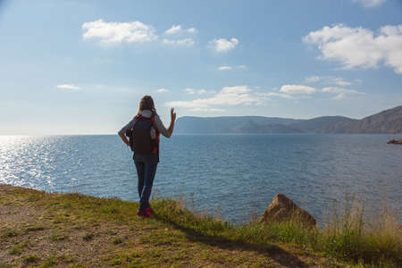 A young female traveler. A girl with a backpack is standing on the seashore. beautiful spring landscape. The concept of tourism, recreation, unity with nature, enjoyment of beauty. active lifestyleの写真素材