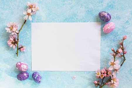 Happy Easter. Easter composition of colored eggs and almond flowers on a blue background. The concept of the holiday. Soft flat layout in pastel colors. Top view, copy space. Aesthetic greeting card.の写真素材