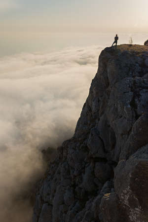 Tourist cliff mountain. Silhouette against the background of bright sunlight. A young man stands on the edge of a cliff. The concept of an active lifestyle, the courage of brave decisions. Travelの写真素材