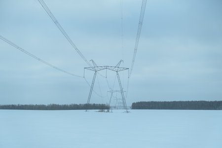 High-voltage poles winter. Electricity for cities. Electric pylons stand in the middle of a snow-covered field. The concept of heating, heating and alternative energy. Winter industrial landscapeの写真素材