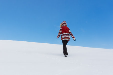 Snowy landscape of a tourist. A winter fairy tale with snow-covered Christmas trees. A woman in a multicolored jacket climbs a mountain against a blue sky. The concept of adventure, active lifestyleの写真素材