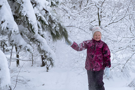 Child snow is having fun. A little girl in a winter forest. He throws snow from the fir branches and laughs. The concept of childhood, carelessness and winter fun. Adventures in the winter forest.の写真素材