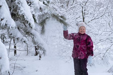 Child snow is having fun. A little girl in a winter forest. He throws snow from the fir branches and laughs. The concept of childhood, carelessness and winter fun. Adventures in the winter forest.の写真素材