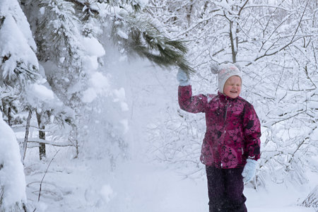 Child snow is having fun. A little girl in a winter forest. He throws snow from the fir branches and laughs. The concept of childhood, carelessness and winter fun. Adventures in the winter forest.の写真素材