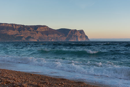 Sea sand evening. Blue post-sunset hour on the seashore. The last rays of the sun are reflected in the waves. Glowing sea foam rolls onto the beach. The concept of summer vacation, relaxation, privacyの写真素材
