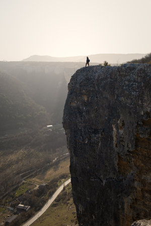Tourist cliff mountain. Silhouette against the background of bright sunlight. A young man stands on the edge of a cliff. The concept of an active lifestyle, the courage of brave decisions. Travelの写真素材