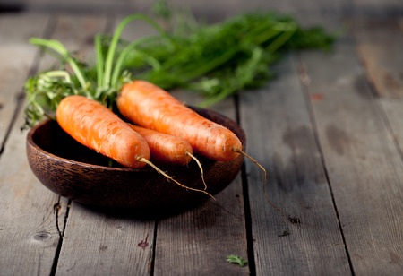Fresh carrots in a wooden bowl on a wooden tableの写真素材