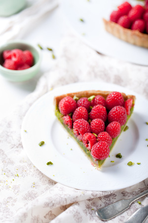 Fresh raspberry and pistachio cream tart on a white textile background.の写真素材