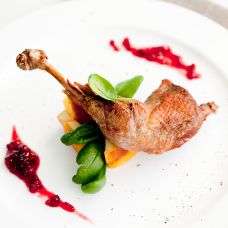 Roasted partridge, chicken thigh with queen apple and spinach leaves on a white plate.の写真素材