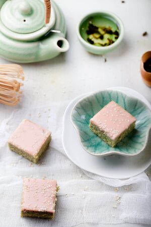Matcha green tea cakes with white chocolate glaze and sesame seeds with a cup of green tea and balm, mint leaves on a wooden backgroundの写真素材