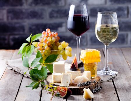 Cheese plate with honey, nuts and grape and white and red wine in glasses on a wooden backroundの写真素材