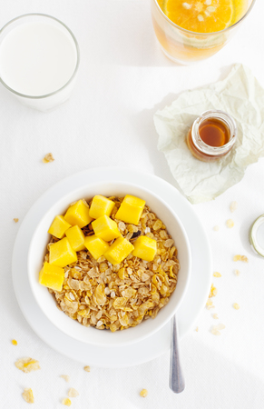 Healthy breakfast. Corn flakes, muesli, granola with mango cubes with a glass of milk and fresh orange juice on a white textile backgroundの写真素材