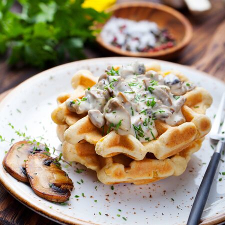 Savory waffles with corn and mushroom creamy sauce on a plate on a wooden backgroundの写真素材