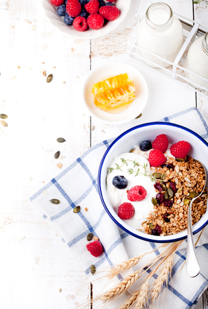 Granola with pumpkin seeds, honey, yogurt and fresh berries in a ceramic bowl on white background.の写真素材