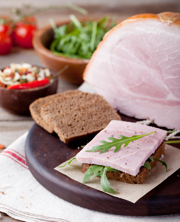 Pork ham on a wooden cutting board with fresh salad and vegetables.の写真素材