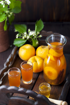 Apricot and cinnamon homemade liquor on a dark wooden background with fresh flowersの写真素材