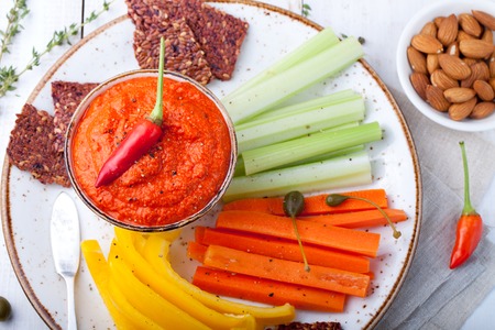 Roasted pepper dip, sauce, spread in a ceramic bowl with fresh carrot, celery sticks on a white wooden backgroundの写真素材